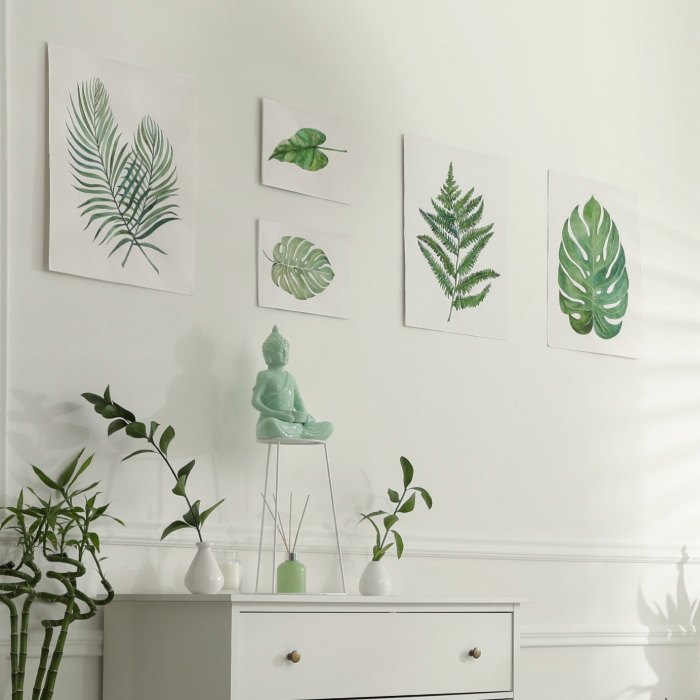 Ambiente decorado em estilo minimalista com parede branca, quadros de folhas verdes, estátua de Buda sobre pedestal, plantas de bambu e aparador branco com pequenos vasos e difusor de aromas.