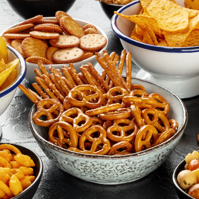 Salgadinhos variados com pretzels, palitos crocantes, biscoitos e chips servidos em diferentes recipientes.