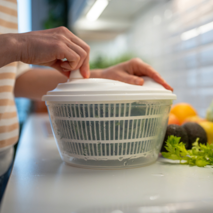 Pessoa utilizando centrífuga de salada para secar folhas verdes frescas na bancada da cozinha.