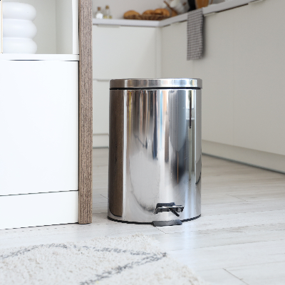 Lixeira de chão com pedal e acabamento metálico posicionada em cozinha com móveis claros.