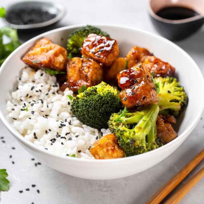 Tigela com arroz branco, brócolis e cubos de tofu caramelizado, decorado com gergelim preto