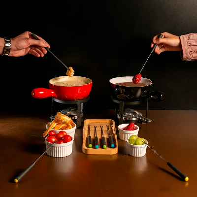 Conjunto de fondue com duas panelas, garfos e acompanhamentos dispostos sobre a mesa.