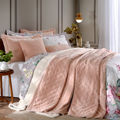 Cobertor rosa com acabamento macio sobre cama arrumada com roupa de cama floral.