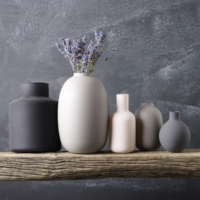 Conjunto de vasos de cerâmica em tons neutros sobre uma madeira rústica, com flores secas de lavanda em destaque no vaso central.