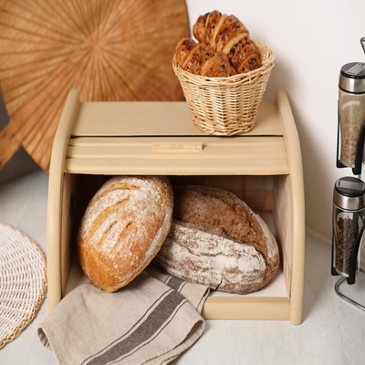 Porta pão de bambu com abertura frontal contendo pães artesanais, decorando uma bancada de cozinha com cesto de pães e porta-condimentos.