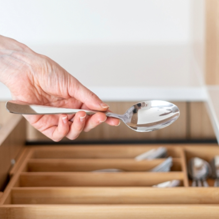 Pessoa segurando uma colher de inox enquanto abre uma gaveta com divisórias para talheres em uma cozinha moderna.
