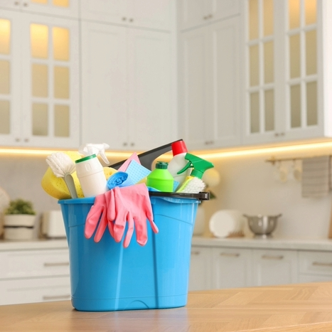 Balde azul com itens de limpeza, como luvas, esponjas e produtos multiuso, sobre bancada de cozinha.