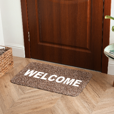 Capacho de porta marrom com escrita “WELCOME” em branco, posicionado em frente à porta de madeira.