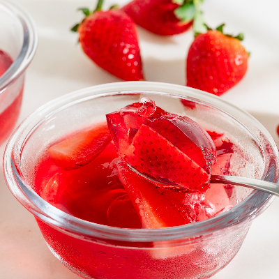 Gelatina de morango vermelha com pedaços de fruta, servida em recipiente de vidro.