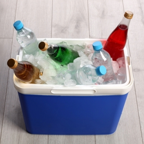 Caixa térmica azul cheia de gelo, contendo garrafas de água e refrigerantes de diferentes cores, disposta sobre um piso de madeira.