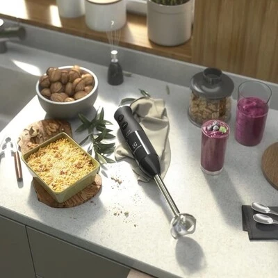 Mixer portátil sobre a bancada da cozinha ao lado de ingredientes e bebidas, ideal para misturar, triturar e preparar receitas com praticidade.