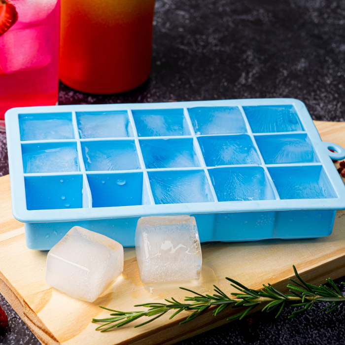 Forma de silicone azul com cubos de gelo, colocada sobre uma tábua de madeira, com dois cubos de gelo e um ramo de alecrim ao lado.
