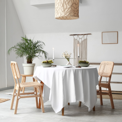 Toalha de mesa redonda branca em sala de jantar clara, com mesa posta e cadeiras de madeira.