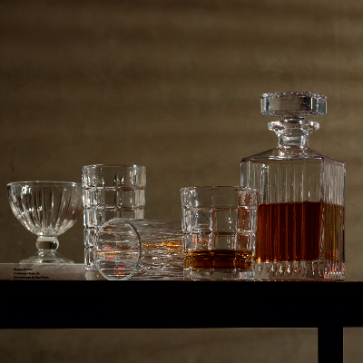 Copos de cristal lapidado acompanhados de decanter com bebida, dispostos sobre mesa em ambiente sofisticado.