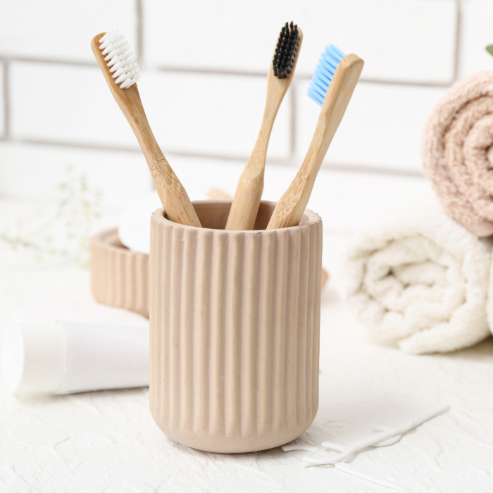 Porta escova de dente bege com textura canelada, acompanhado de escovas de bambu em um ambiente claro e aconchegante.