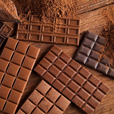 Diferentes barras de chocolate ao leite e chocolate amargo dispostas sobre superfície de madeira com cacau em pó.