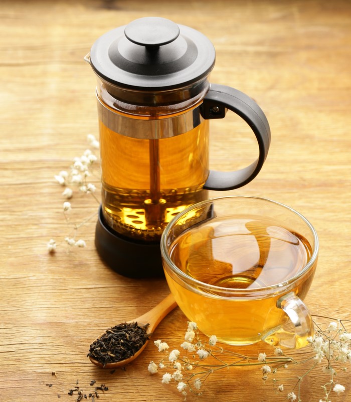 uma cafeteira francesa com chá, uma xícara e uma colher