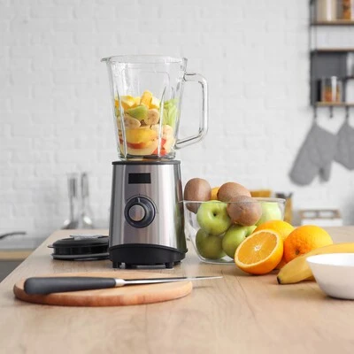 Liquidificador com frutas frescas na cozinha Liquidificador com copo de vidro contendo frutas variadas sobre bancada de madeira, cercado por laranjas, maçãs, kiwis e bananas em cozinha moderna.Liquidificador com frutas frescas na cozinha