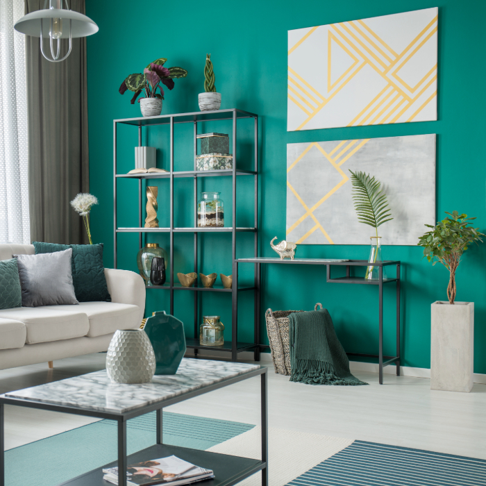 Sala de estar moderna com parede verde, sofá branco decorado com almofadas em tons de verde e cinza, estante metálica com objetos decorativos, mesa de centro com tampo marmorizado e quadros geométricos amarelos na parede.