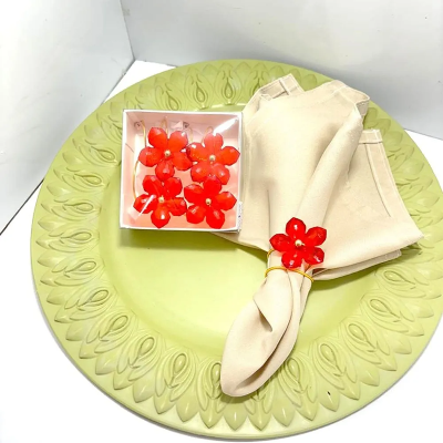Argola para guardanapo dourada com flor vermelha decorativa, envolvendo guardanapo bege sobre prato verde com detalhes em relevo.