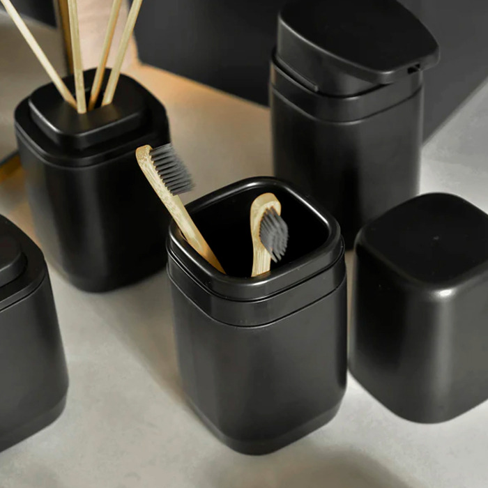 Porta escova de dente preto com tampa, em ambiente moderno, contendo escovas de bambu com cerdas pretas.
