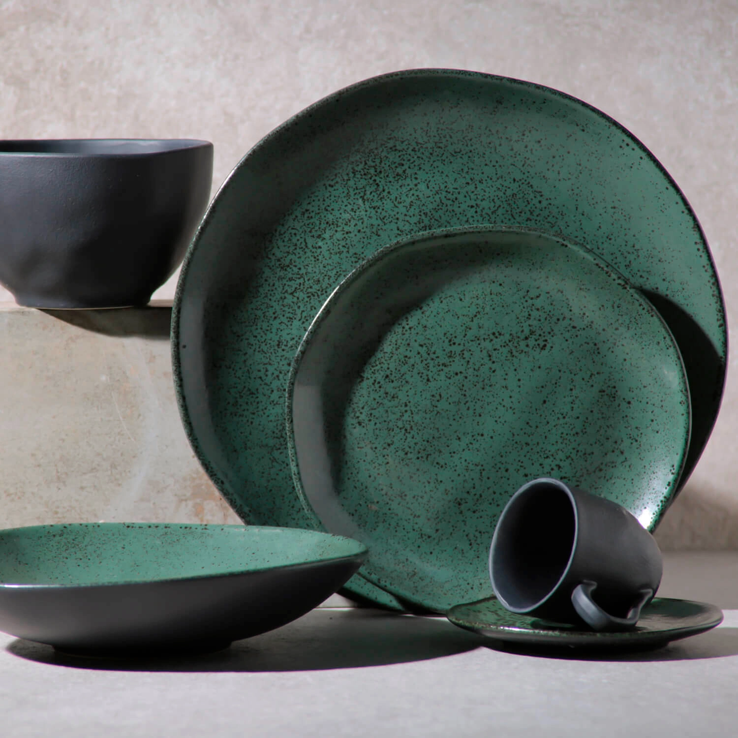 Prato de cerâmica verde com efeito esmaltado e acabamento artesanal, acompanhado de bowl e xícara em uma composição moderna.