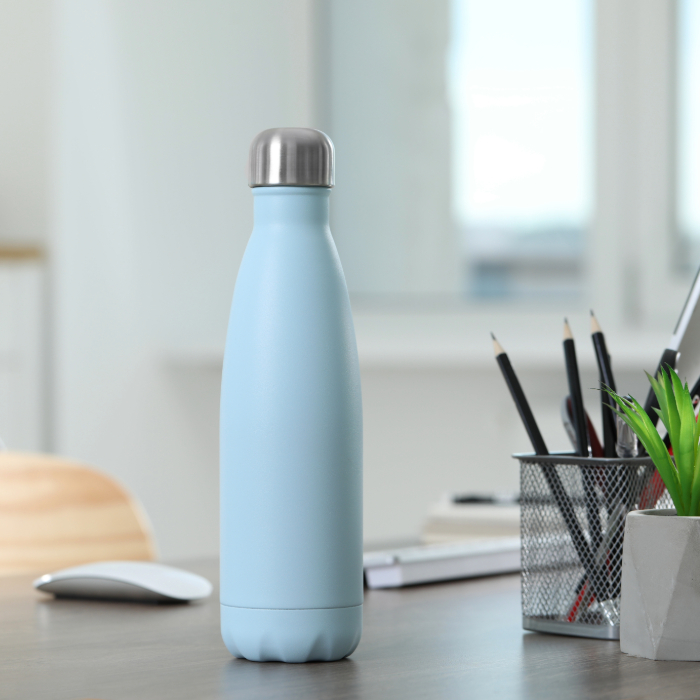 Garrafa térmica azul claro com tampa de inox sobre uma mesa de escritório, ao lado de materiais de papelaria.
