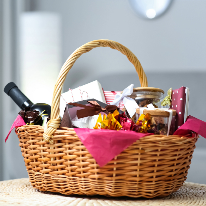 Cesta de presente de vime com vinho, doces, potes e embalagens coloridas, ideal para ocasiões especiais.