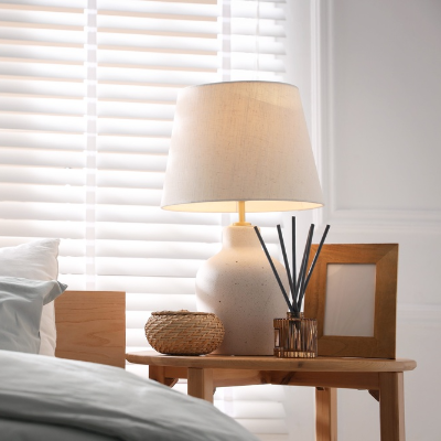 Difusor de ambiente com varetas sobre mesa de cabeceira, ao lado de luminária e objetos decorativos.