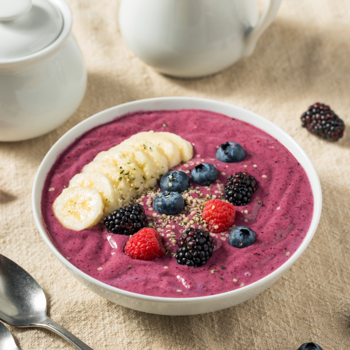 Tigela de smoothie roxo decorada com fatias de banana, mirtilos, framboesas, amoras e sementes