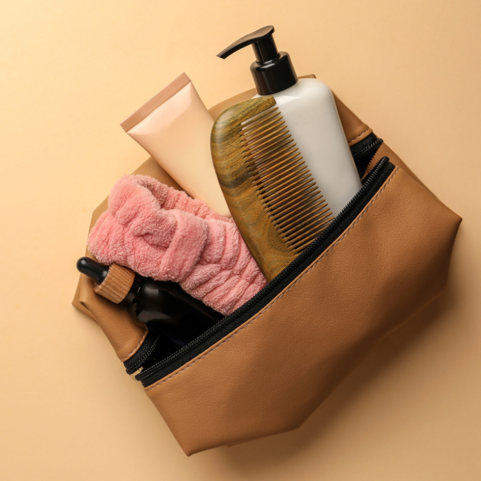Necessaire bege com zíper contendo escova, frascos e itens de higiene pessoal sobre fundo bege.