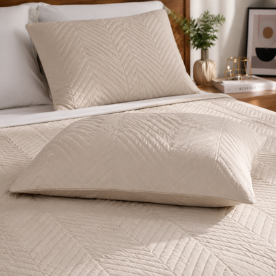 Fronha bege matelassê em destaque sobre cama com colcha combinando e decoração moderna.