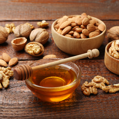 Nuts com amêndoas e nozes acompanhadas de mel, dispostas sobre mesa de madeira.