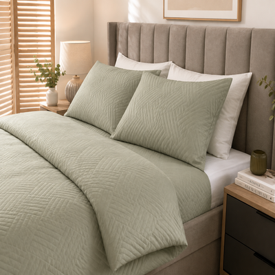 Fronhas verdes em cama posta com colcha combinando, cabeceira estofada e decoração moderna.