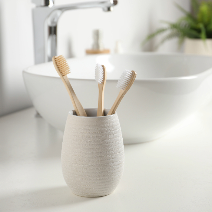 Porta escova de dente branco com acabamento fosco ao lado de uma cuba de banheiro, com escovas de bambu com cerdas brancas.