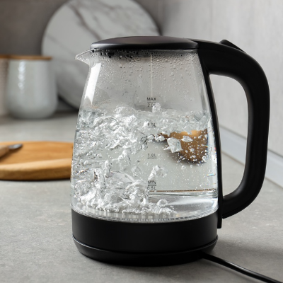 Chaleira elétrica de vidro transparente com água fervendo, base e alça pretas, sobre bancada de cozinha.