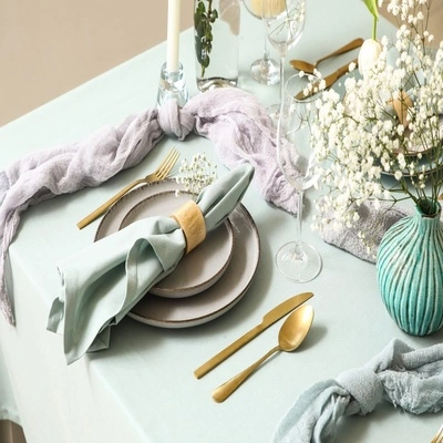 Mesa posta elegante com louças em tons neutros, guardanapo verde, talheres dourados, taças e arranjos florais delicados em uma decoração sofisticada.
