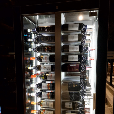 Adega climatizada com porta de vidro e diversas garrafas de vinho armazenadas horizontalmente em compartimentos internos.