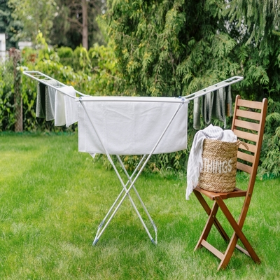 Varal portátil de chão com estrutura metálica e roupas secando em jardim, oferecendo praticidade, ventilação e economia de espaço.