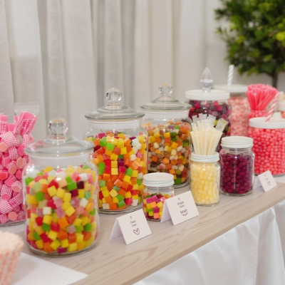 Balas e chicletes de diferentes cores e formatos organizados em potes de vidro para mesa de doces.