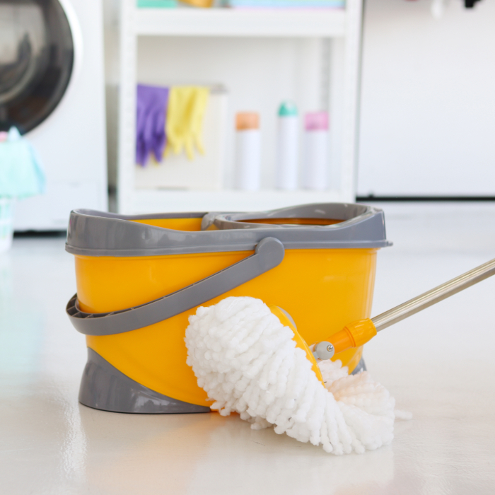 Balde amarelo com sistema de esfregão giratório e mop branco, em ambiente de lavanderia.