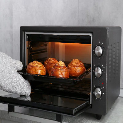 Forno elétrico de bancada preto aberto com alimentos assando em assadeira.