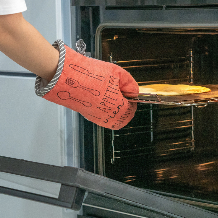 Pessoa usando uma luva térmica vermelha para retirar uma assadeira do forno com uma pizza.