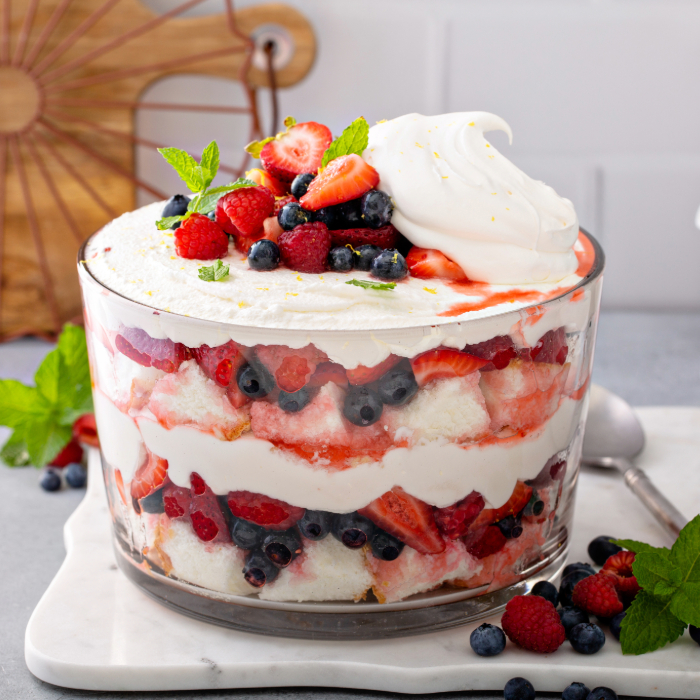 Sobremesa em camadas de chantilly, frutas vermelhas e bolo, servida em uma tigela de vidro e decorada com frutas frescas no topo.