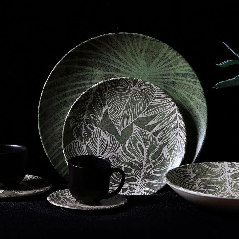 Prato de cerâmica estampado com folhas em tons de verde, combinado com bowl e xícara, criando uma mesa posta elegante e contemporânea.