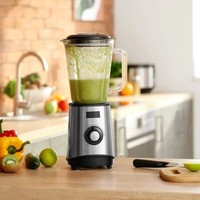 Liquidificador com suco verde saudável Liquidificador em funcionamento com bebida verde no copo de vidro, posicionado sobre bancada de madeira com frutas e vegetais ao redor.