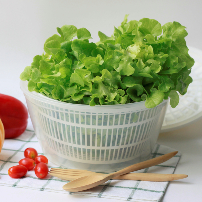 Folhas de alface frescas em centrífuga de salada, com utensílios de madeira e tomatinhos ao lado.