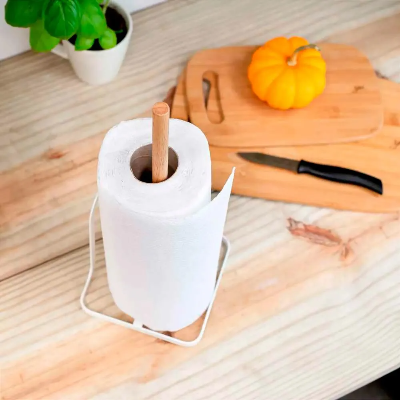 Suporte para papel-toalha branco com haste central de madeira, acomodando um rolo de papel sobre uma bancada de cozinha com utensílios ao fundo.