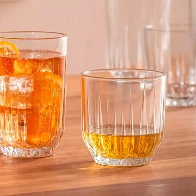 Copos de vidro para whisky com bebida âmbar e gelo sobre mesa de madeira em ambiente aconchegante, ideais para servir drinks e destilados.