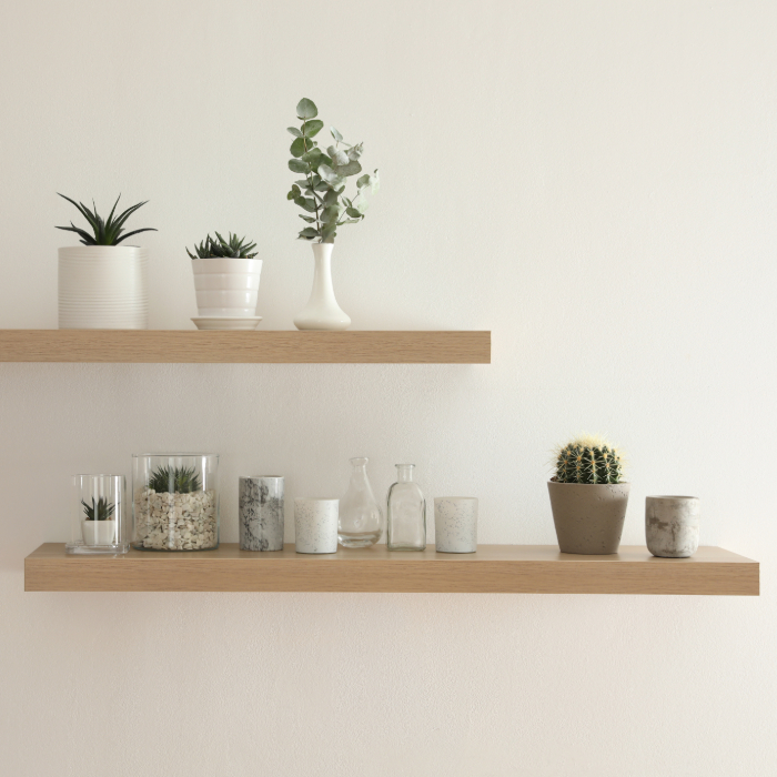 Prateleiras de madeira minimalistas fixadas em parede branca, decoradas com pequenos vasos de plantas suculentas e cactos, velas decorativas e garrafas de vidro.